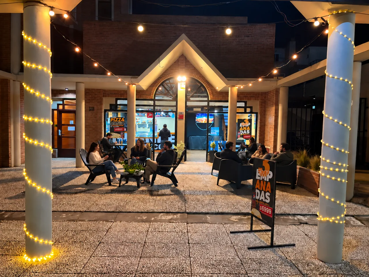 Terraza de Big Pizza Pinamar iluminada por la noche y con mesas ocupadas